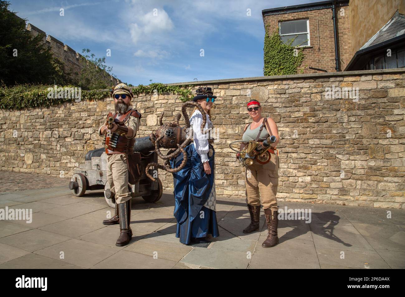 Steampunks richten ihre Waffen auf die Kamera. Ein weiblicher Steampunk trägt einen großen Kupferoktopus auf dem Rücken. Stockfoto