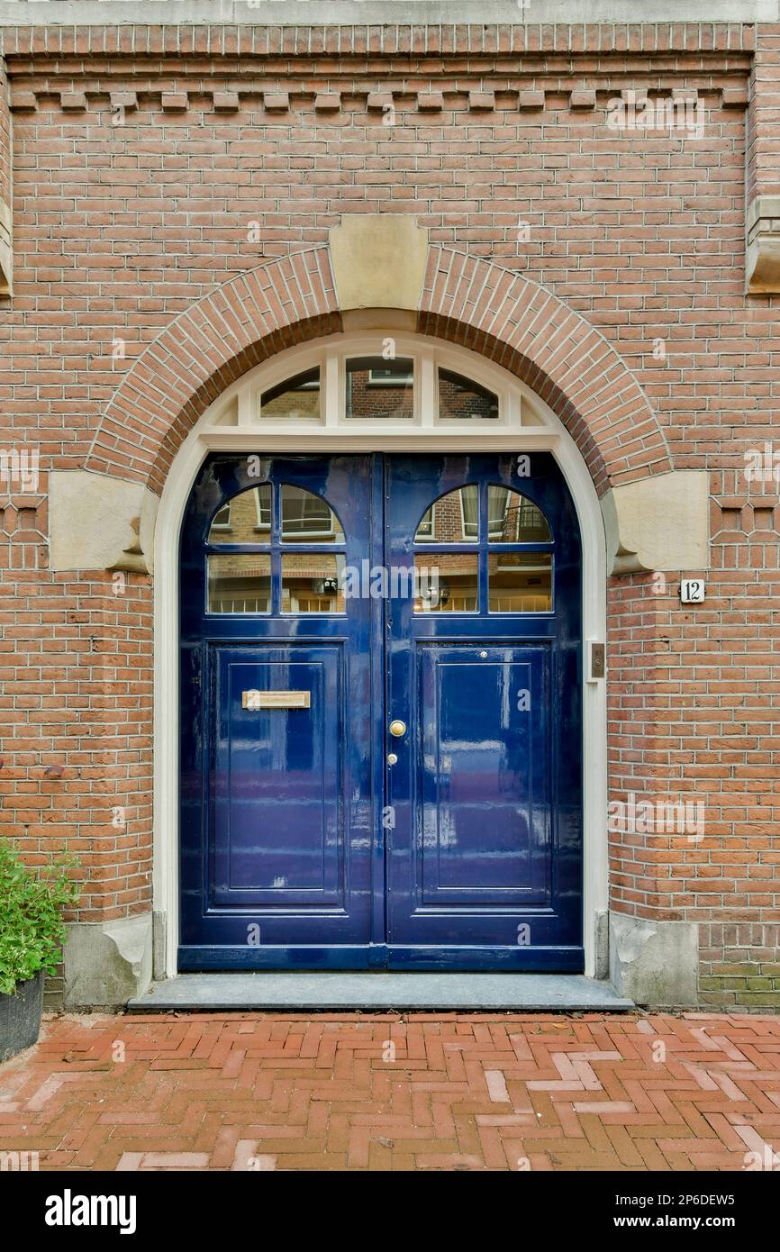 Eine blaue Tür vor einem roten Backsteingebäude mit einem Bogenfenster darüber und die Türen sind offen Stockfoto