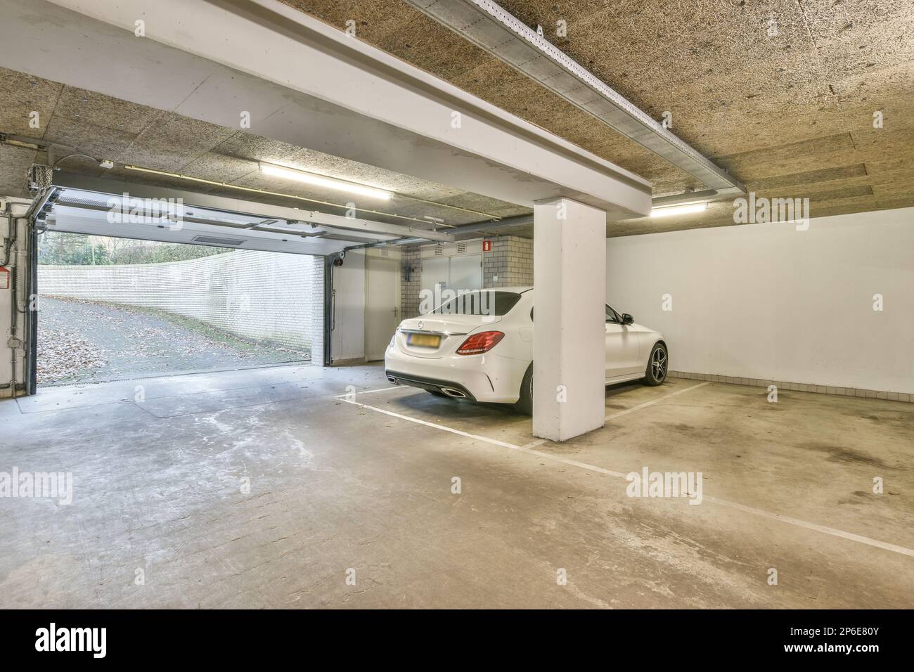 Ein weißes Auto parkt in einer Garage mit einer offenen Tür auf der einen Seite und der anderen Hälfte des Fahrzeugs Stockfoto