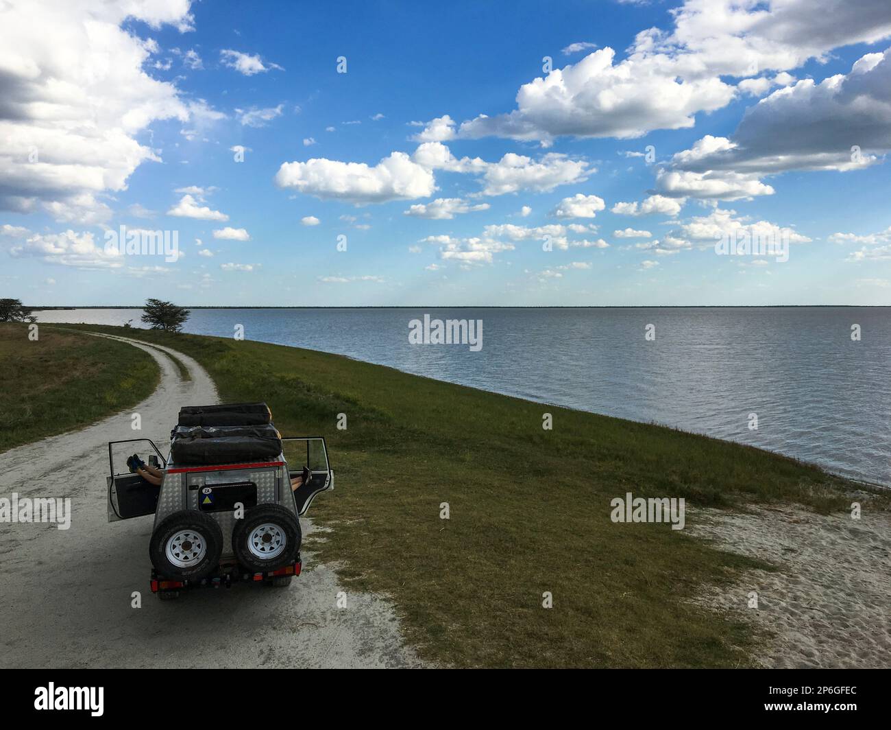 2 junge Erwachsene stehen auf einem Jeep als Silhouetten, die menschliche Figuren spielen. Sturmwolken am Himmel. Makgadikgadi Salzwannen, Botsuana, Afrika Stockfoto