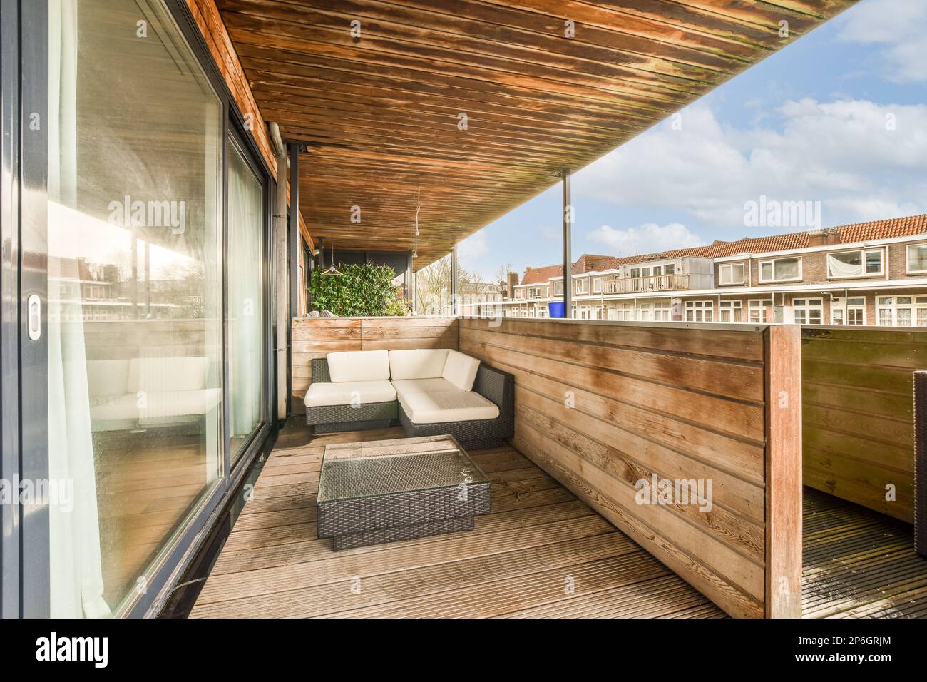 Ein Wohnbereich im Freien mit Holzfußboden und weißen Sofas auf einer Holzterrasse vor einer Reihe von Häusern Stockfoto