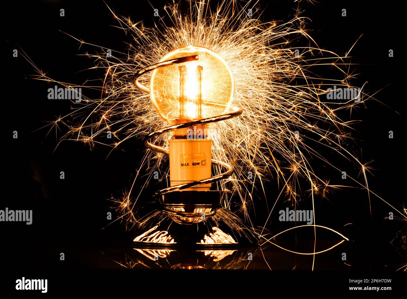 Isolierte, beleuchtete Glühlampe mit Brandfunken und Glühfaden auf schwarzem Hintergrund. Elektrizitätskonzept. Stockfoto
