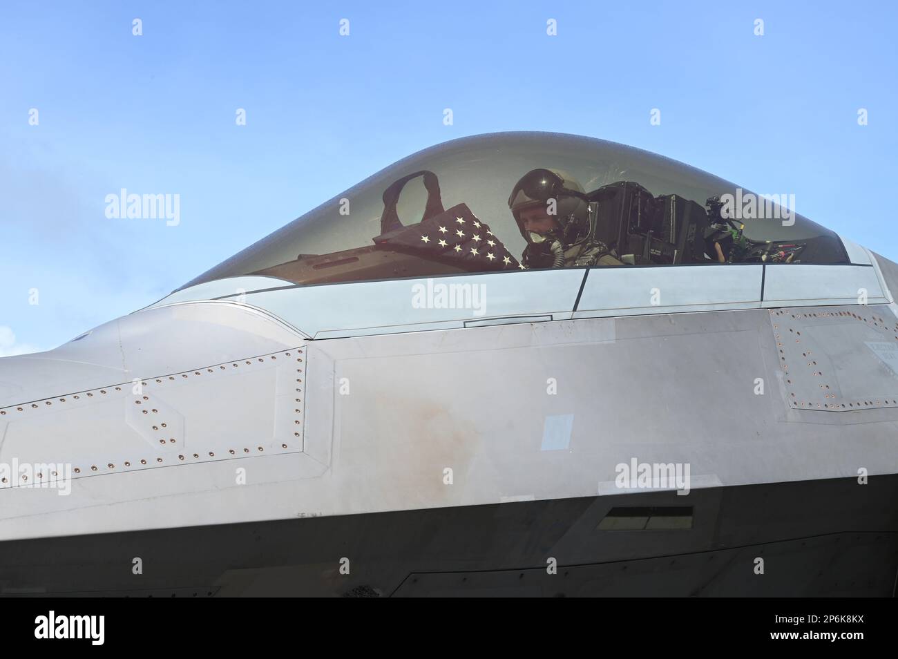Romo, ein F-22 Raptor-Pilot, der der 525. Expeditionary Fighter Squadron zugeteilt wurde, bereitet sich auf das Fliegen einer Trainingssortie vor, während er während der Übung Agile Reaper 23-1 am internationalen Flughafen Tinian, Nördliche Marianen, am 3. März 2023 eine amerikanische Flagge zeigte. Während ihres Aufenthalts in Tinian wurde ein verstorbenes früheres Mitglied des Militärdienstes an ihren Geburtsort zurückgebracht, und die 3. AEW zollte ihr und ihrer Familie ihren Respekt, indem sie die Flagge in einem F-22 Raptor hing und sie der Familie bei der Ankunft des Mitglieds überreichte. (USA Air Force Foto von Tech. Sgt. Hailey Staker) Stockfoto