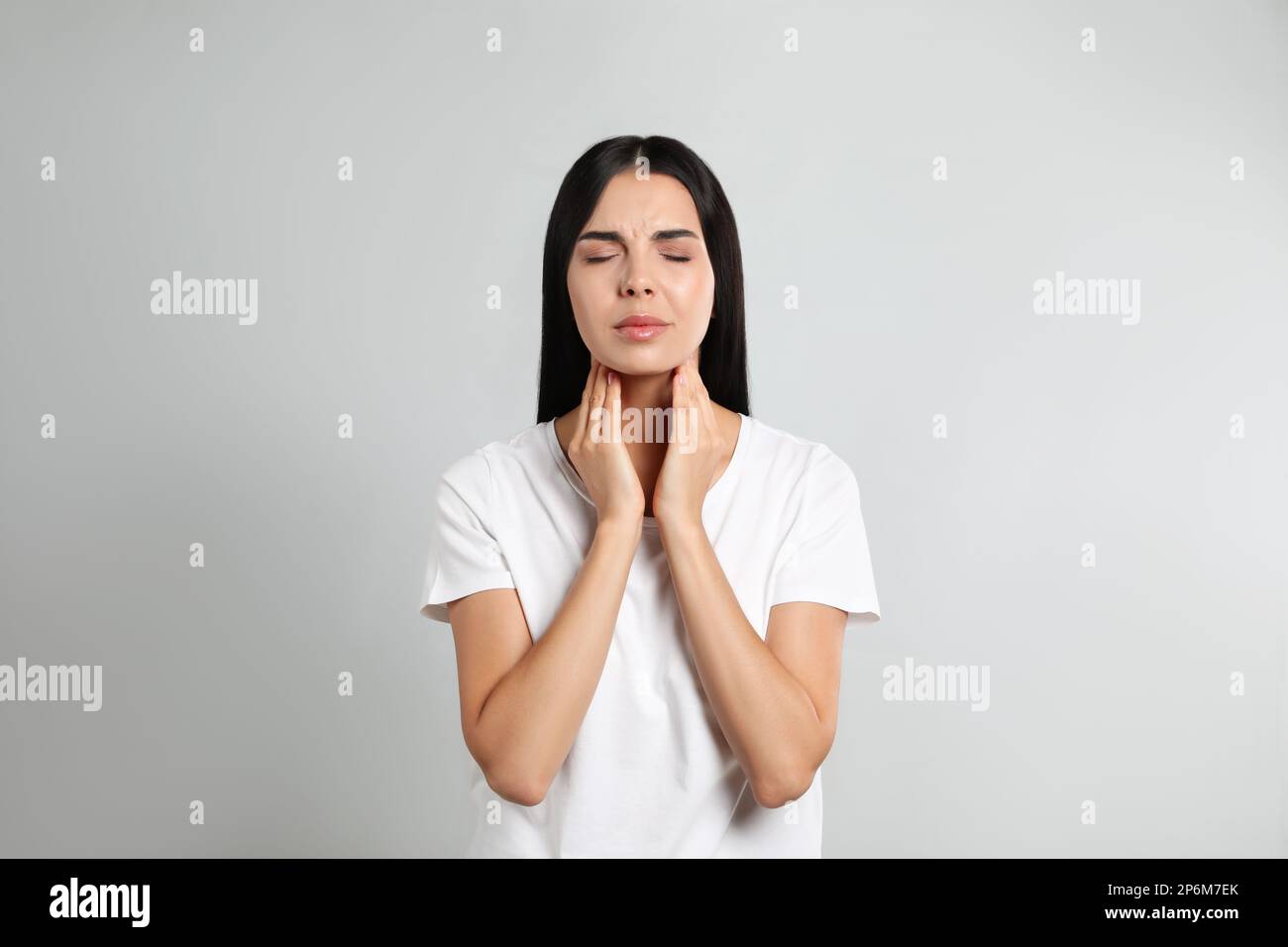 Junge Frau, die Schilddrüsen-Selbstuntersuchung vor hellem Hintergrund durchführt Stockfoto
