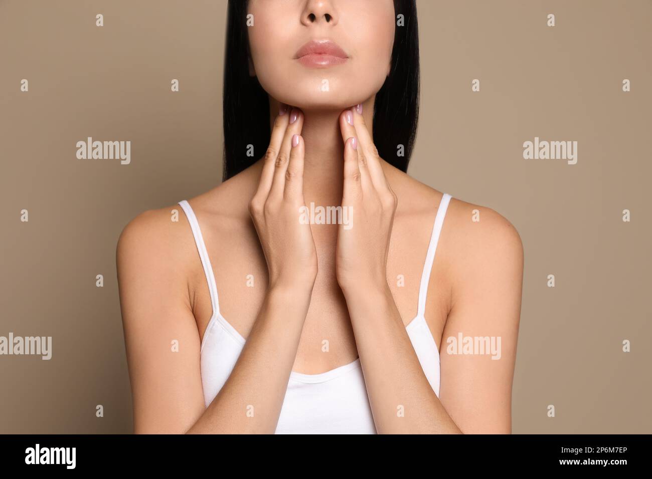 Junge Frau, die Schilddrüsen-Selbstuntersuchung auf beigefarbenem Hintergrund macht, Nahaufnahme Stockfoto