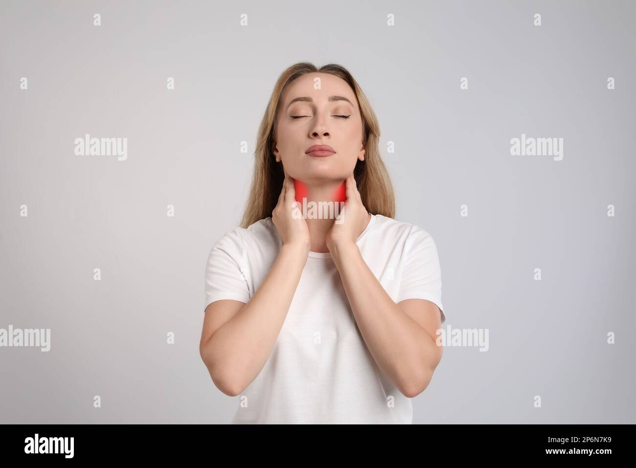 Junge Frau, die Schilddrüsen-Selbstuntersuchung auf hellgrauem Hintergrund durchführt Stockfoto