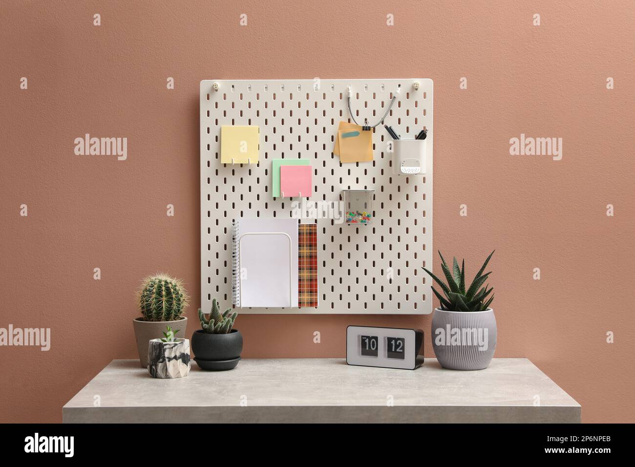 Weiße Notiztafel mit Notizen und Schreibwaren, die an der rosafarbenen Wand über dem Tisch hängen Stockfoto