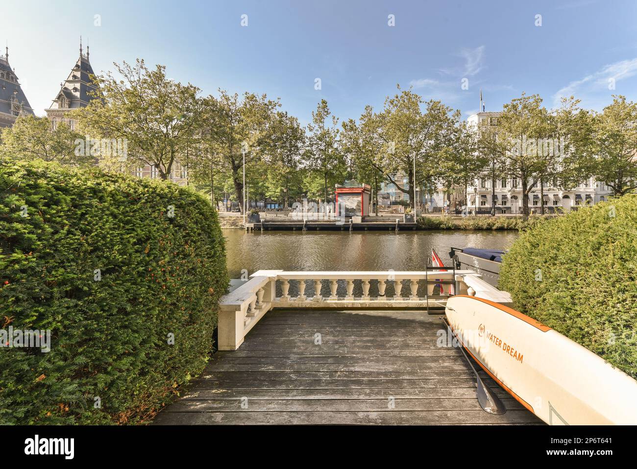 Ein Boot, das am Ende einer hölzernen Anlegestelle vor einem Fluss mit Bäumen und Gebäuden auf beiden Seiten angedockt ist Stockfoto