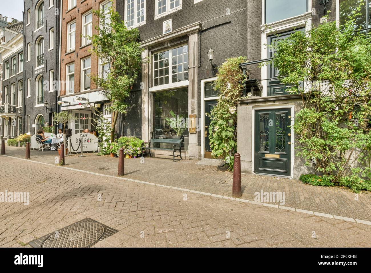 Amsterdam, Niederlande - 10. April 2021: Eine Stadtstraße mit Menschen, die auf Bänken und Tischen in der Mitte der Straße sitzen, umgeben von hohen Ziegelgebäuden Stockfoto