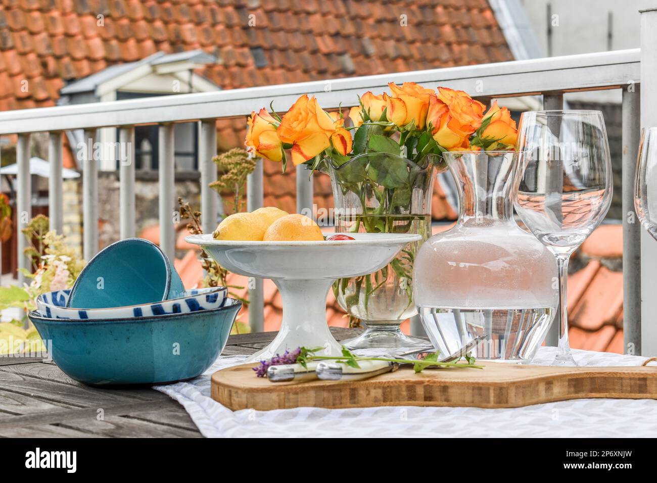 Blumen in Vasen und Teller auf einem Holztisch mit einem orangefarbenen Haus im Hintergrund Stockfoto