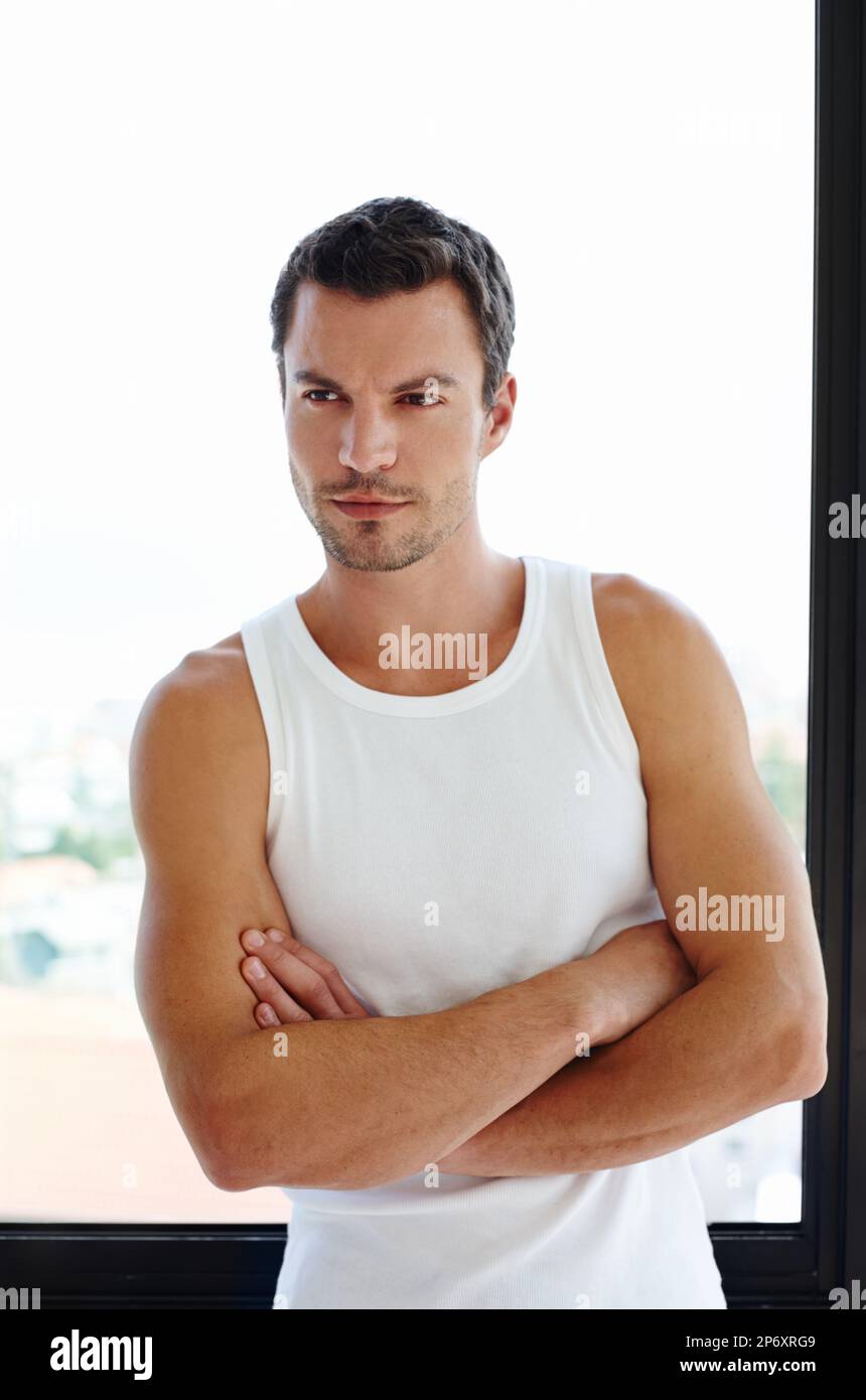 Selbstbewusst in jeder Situation. Ein gutaussehender Mann, der mit gefalteten Armen vor dem Fenster steht. Stockfoto