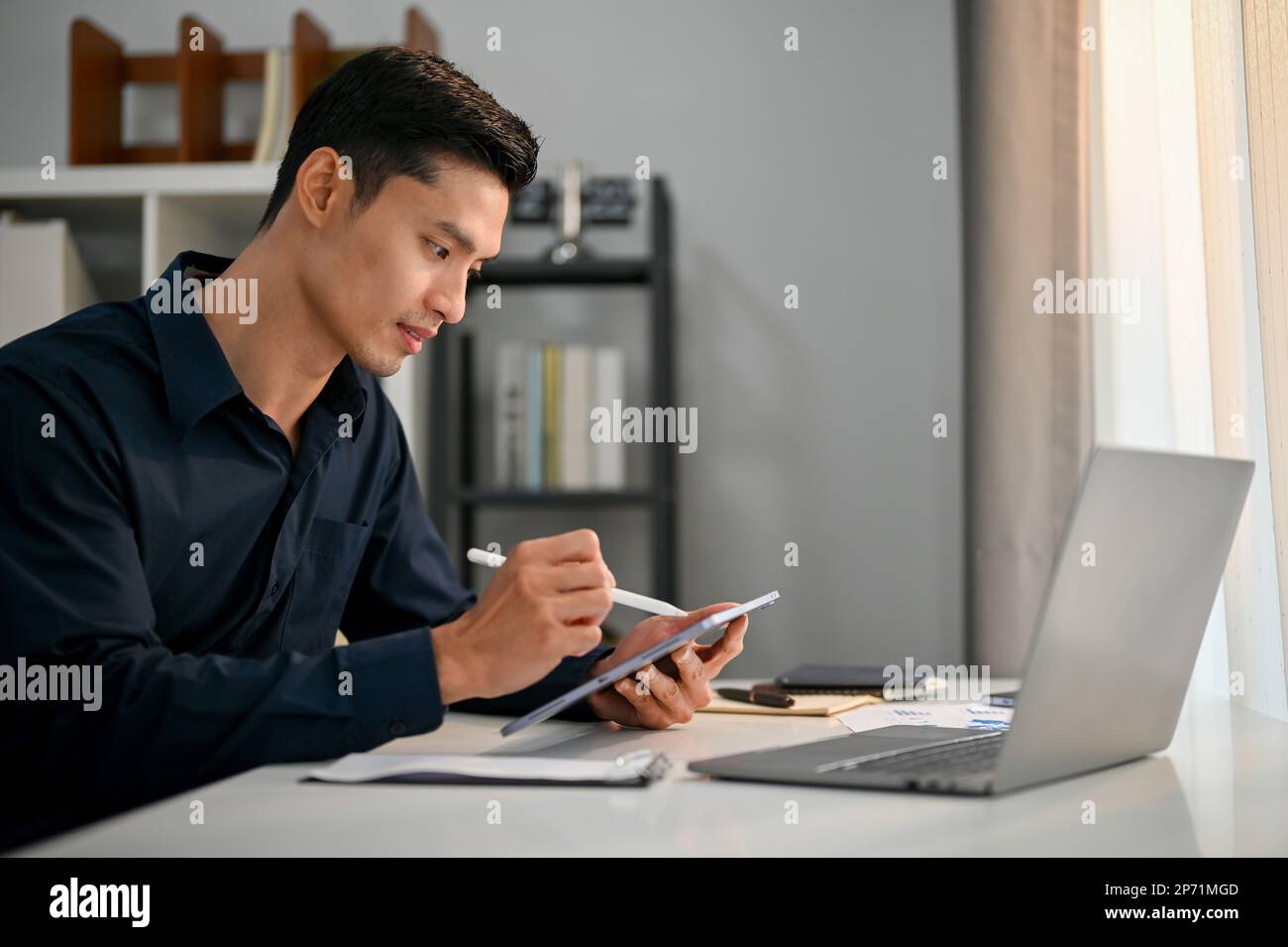 Professioneller und erfolgreicher asiatischer Geschäftsmann oder männlicher Manager, der an seinem Schreibtisch im Büro arbeitet und sein Unternehmen mit einem digitalen Tablet verwaltet Stockfoto