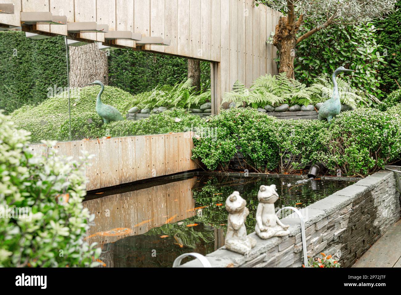 Amsterdam, Niederlande - 10. April 2021: Zwei Katzen sitzen am Rand eines kleinen Teiches vor einem Gebäude mit Bäumen und Pflanzen Stockfoto