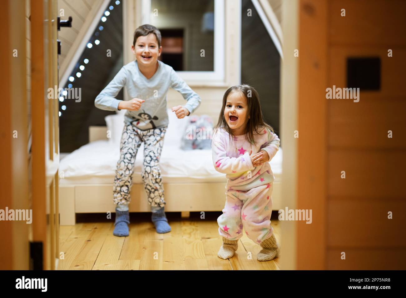 Kinder in weichen, warmen Pyjamas, die in einer Holzhütte spielen. Konzept von Kindheit, Freizeit, Glück. Bruder und Schwester haben Spaß und spielen Stockfoto