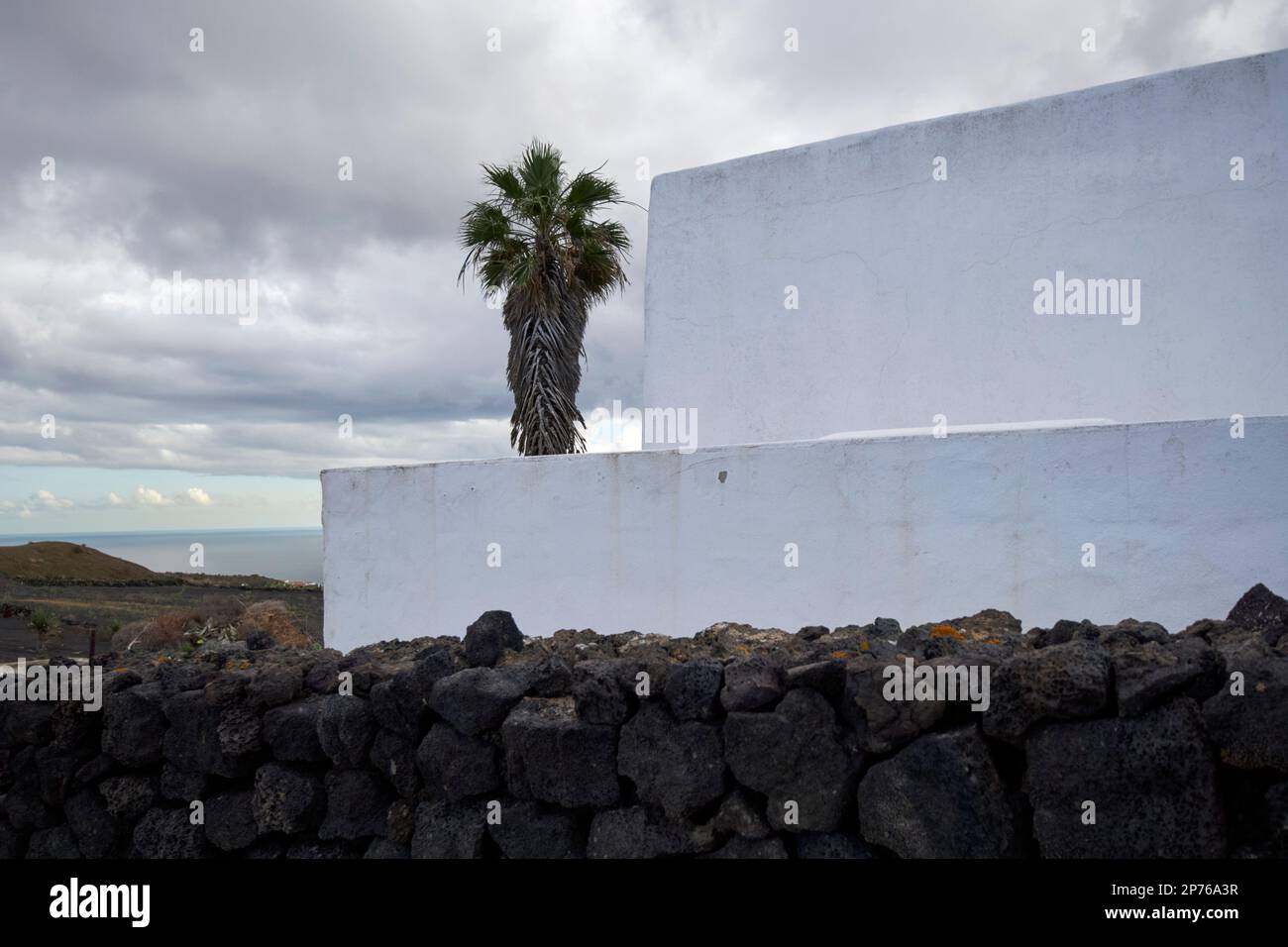 Typische quadratische Konstruktion, weiß getünchte Wände, vulkanische Felswand und Palme eines kleinen Bauernhofs Lanzarote, Kanarische Inseln, Spanien Stockfoto