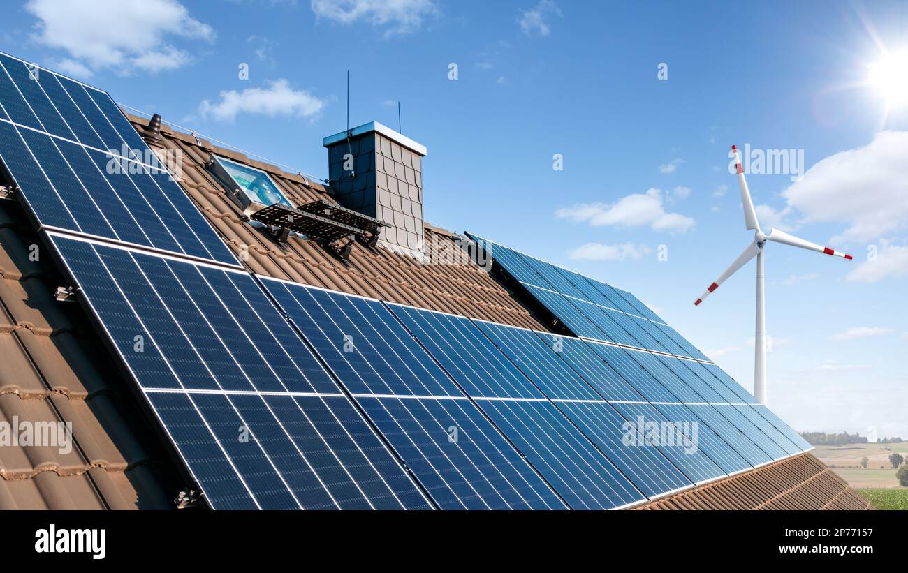 Sonnenkollektoren auf dem Dach eines Familienhauses mit einer Windturbine im Hintergrund Stockfoto