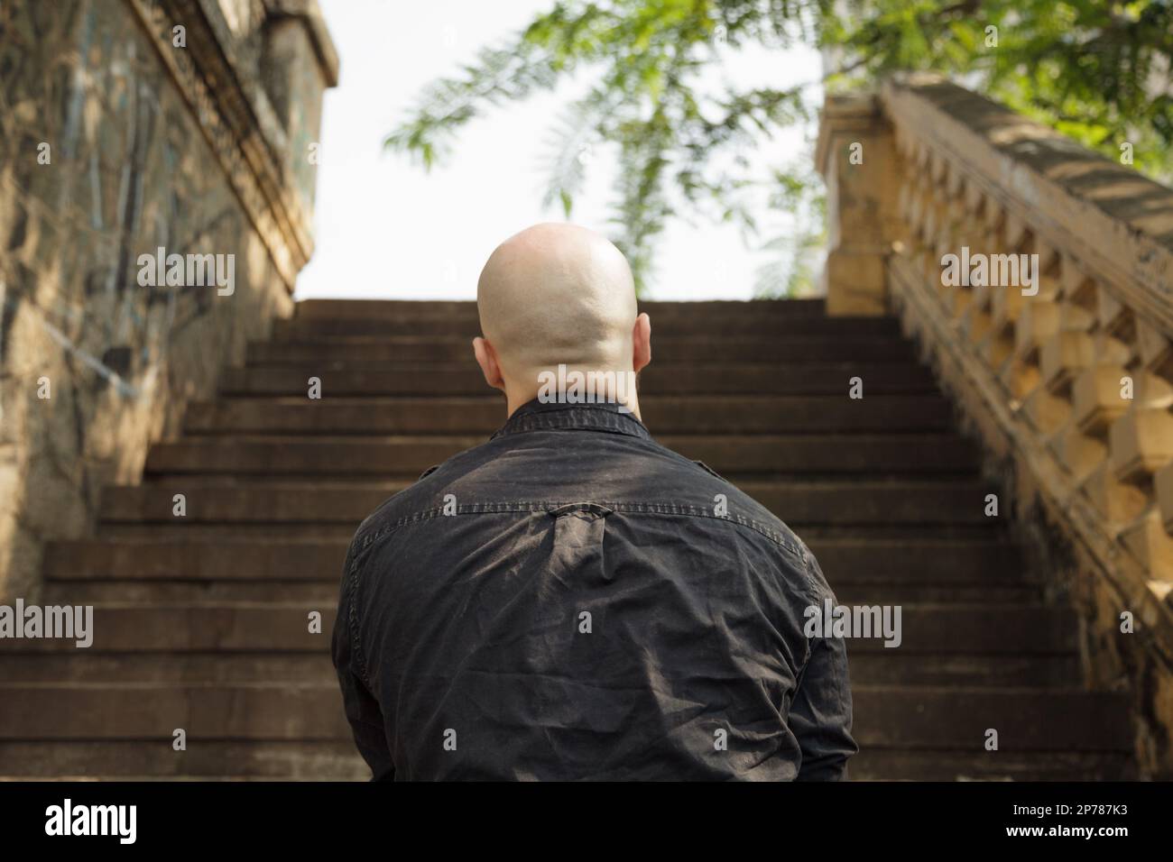 Rückansicht eines kahlköpfigen kaukasischen Mannes, der vor der Treppe steht. Nicht identifiziertes Inkognito-Personenkonzept. Unkenntlich übergewichtige Person, die schaut Stockfoto