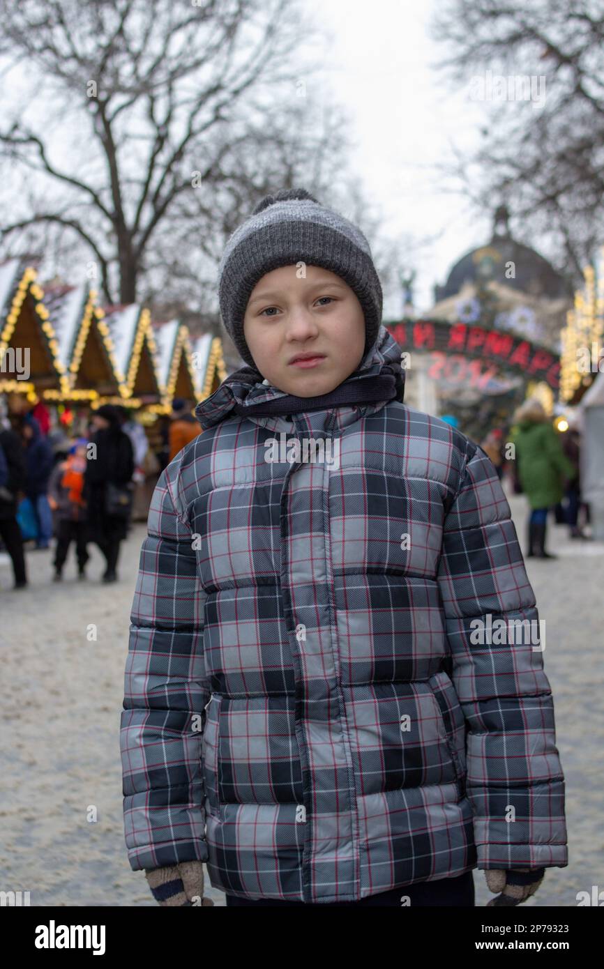 Der kleine traurige Junge steht im Winter auf dem Weihnachtsmarkt Stockfoto
