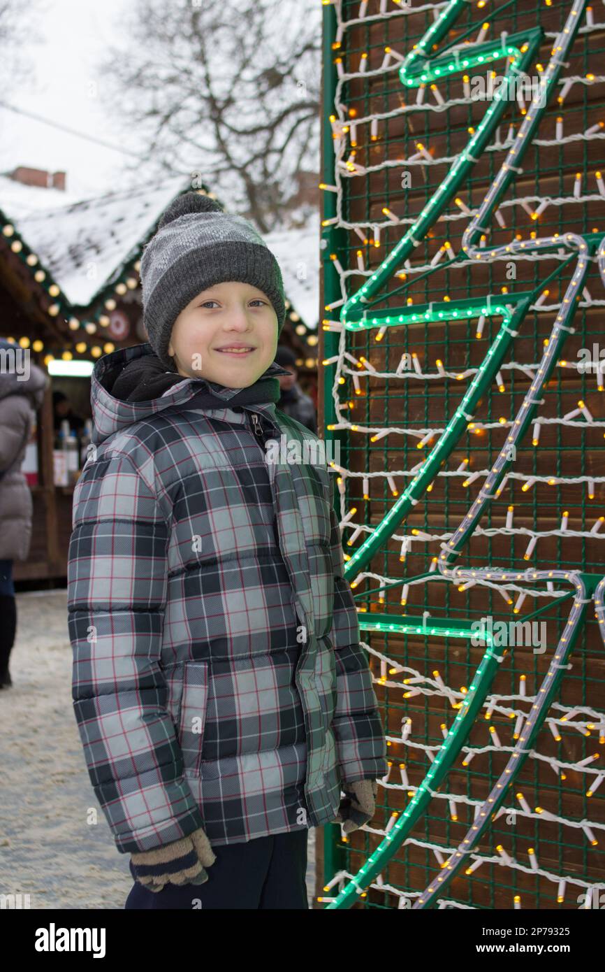 Ein Junge neben einem künstlichen Weihnachtsbaum auf der Straße, glücklich Stockfoto