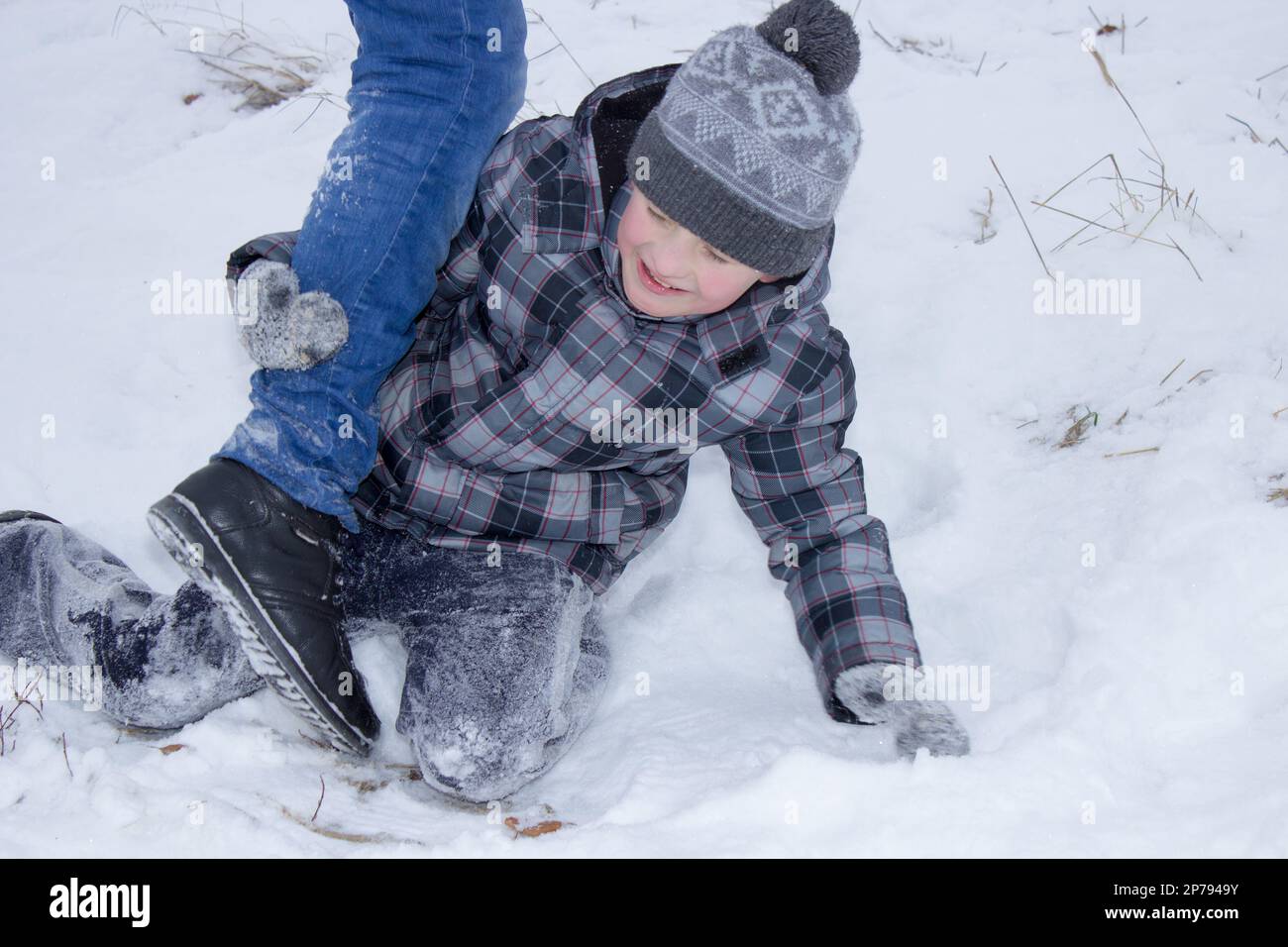 Im Winter tritt ein Teenager einen Jungen, der im Schnee sitzt Stockfoto