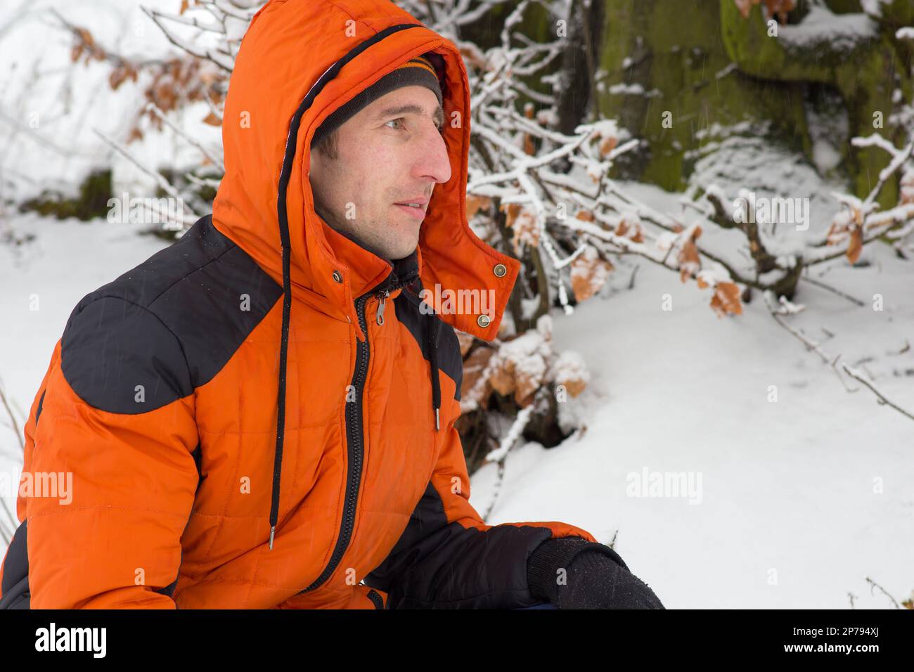 Ein Mann in einer orangefarbenen Sportjacke saß im Schnee Stockfoto