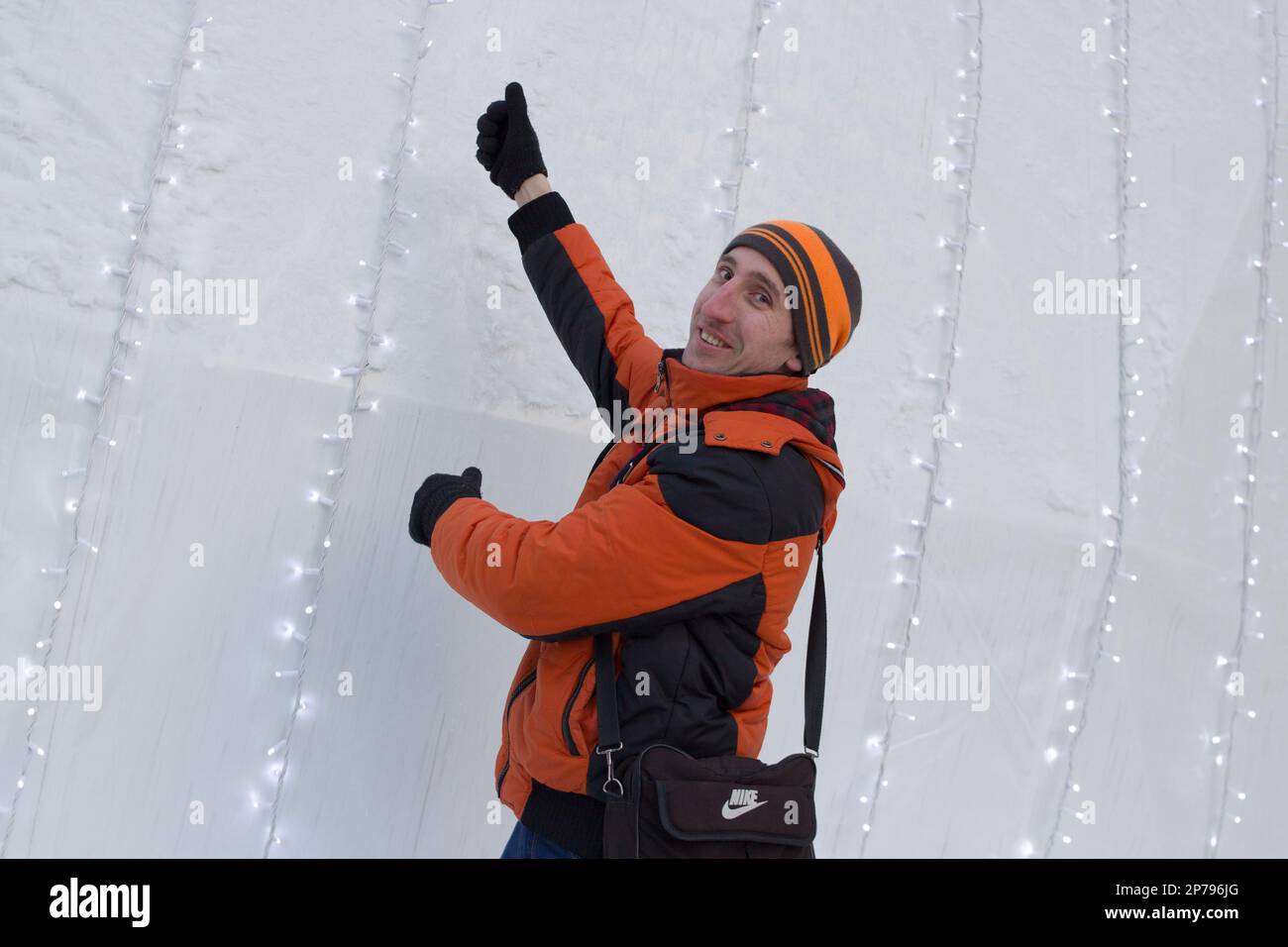 Ein glücklicher Mann in der Winter-orangefarbenen Winterjacke zeigt Hände Stockfoto