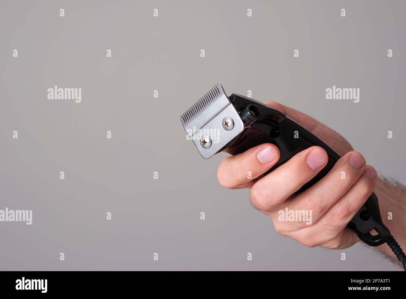 Elektrischer Haarschneider, der von einem männlichen Kaukasier in der Hand gehalten wird Nahaufnahme Vorderansicht isoliert auf Grau. Stockfoto