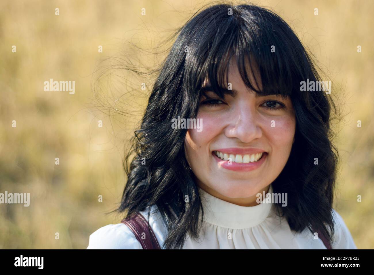Junge lateinische Frau venezolanischer Herkunft, lächelnd mit guten Zähnen, mit kurzen schwarzen Haaren und weißen Kleidern, stand draußen, schaute in die Kamera. Stockfoto