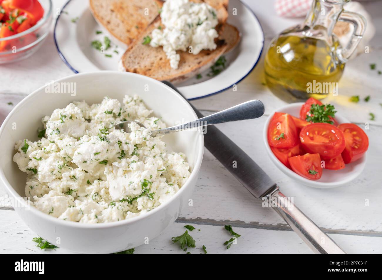 Feta-Käsesalat mit Kräutern und Olivenöl. Serviert mit geröstetem Sauerteigbrot, Tomaten und Paprika auf einem Tisch Stockfoto