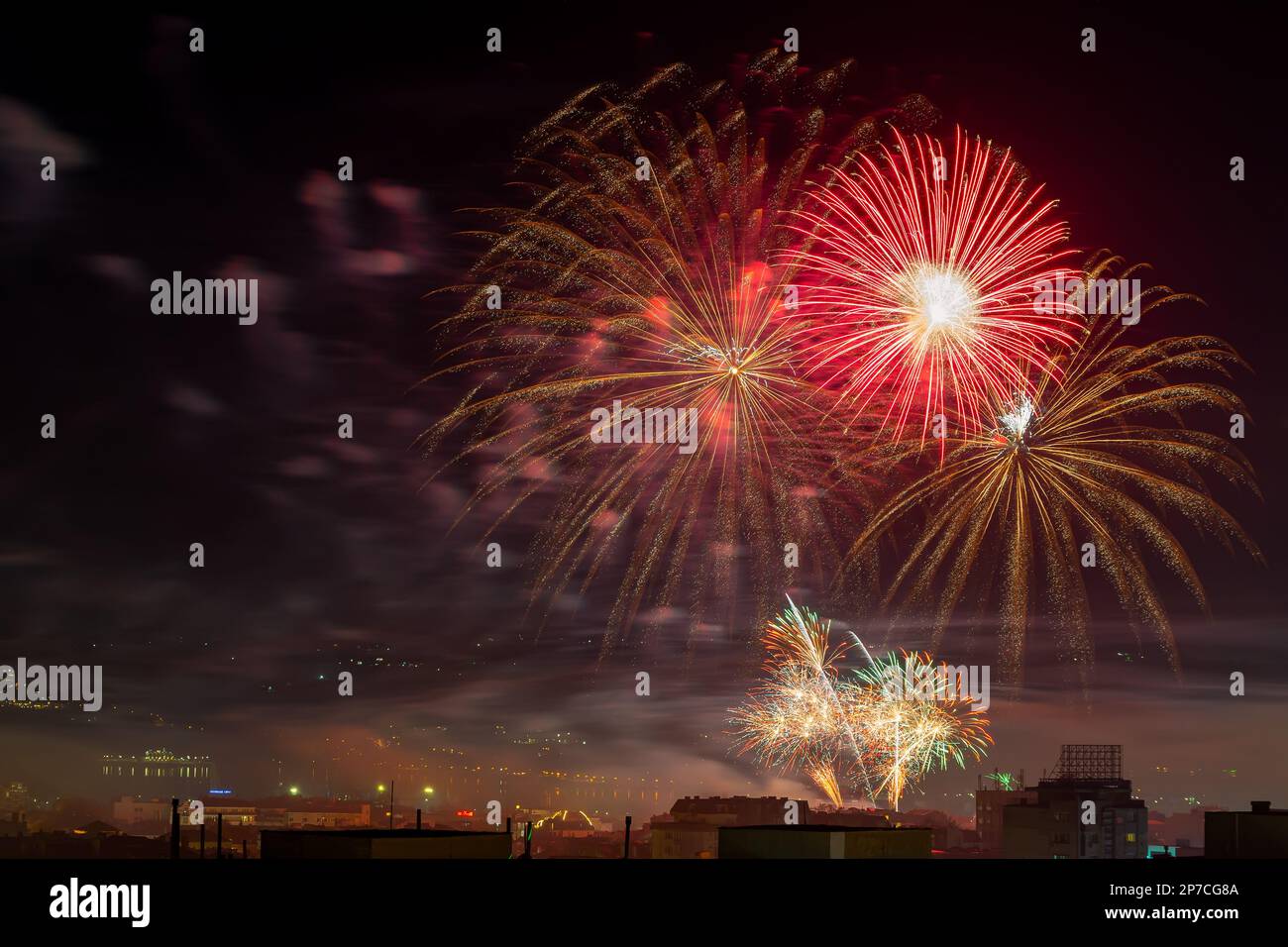 Rote Feuerwerkexplosionen am Mitternachtshimmel. Feiertagsveranstaltung in der Stadt mit einem hellen Feuerwerk bei Nacht. Festliches pyrotechnisches Konzept. Stockfoto