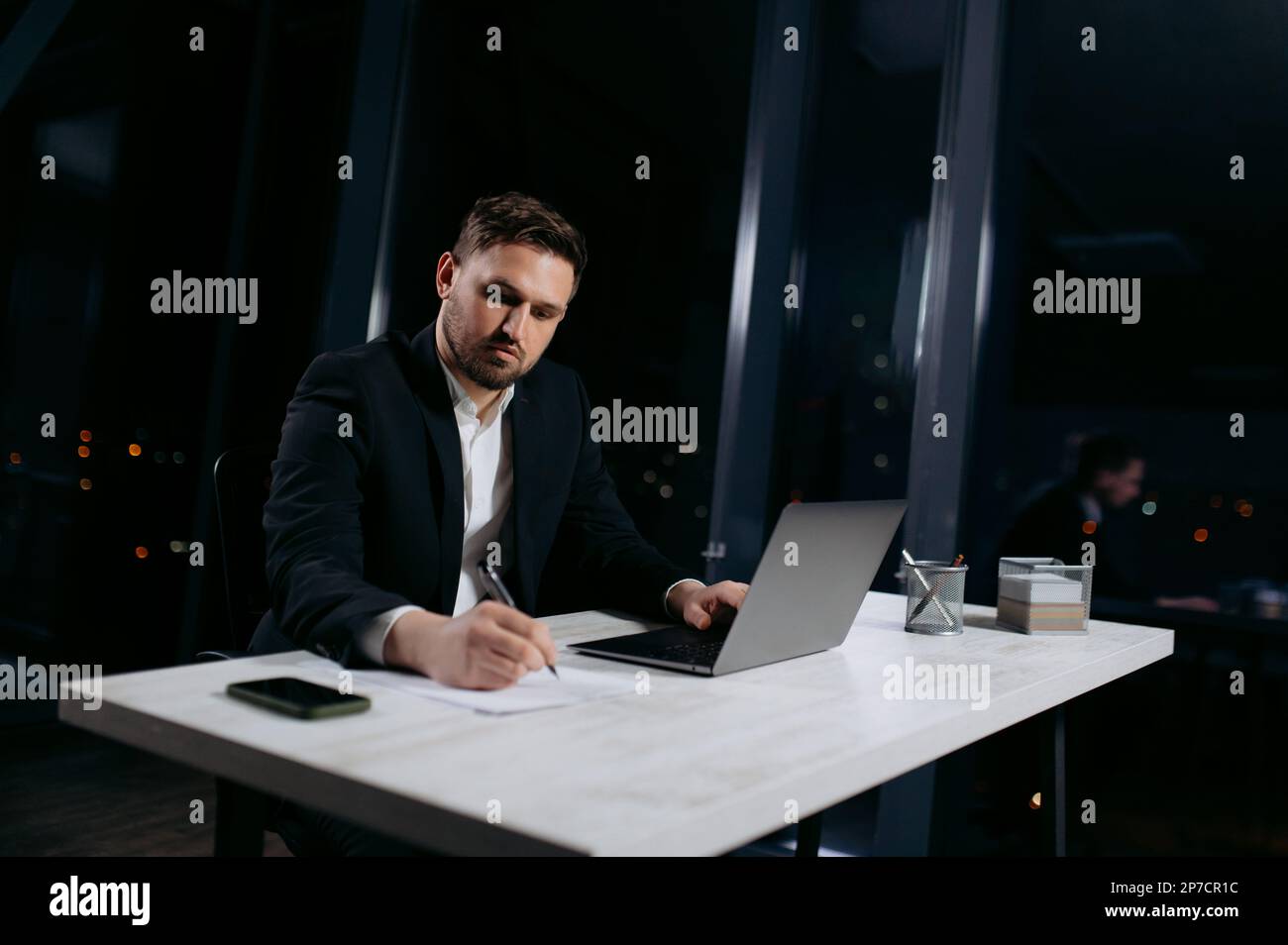 Junger Praktizierender auf dem Roboter, um Notizen zu machen. Der Mann arbeitet abends im Büro Stockfoto