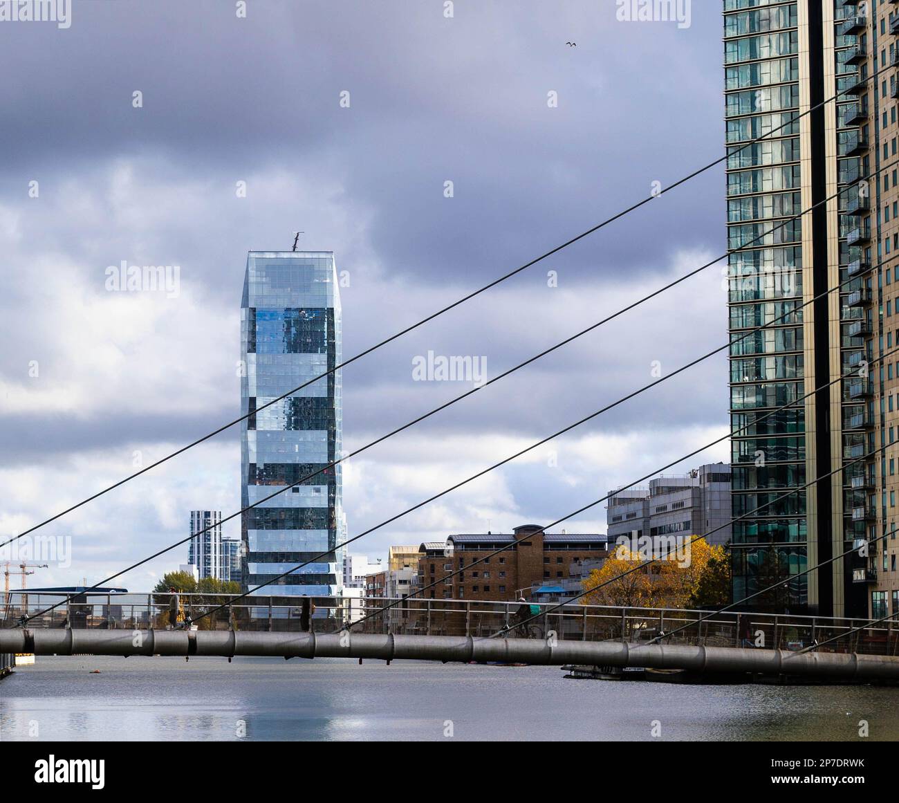 Das Dollar Bay Gebäude, in der Nähe von Canary Wharf, ist über dem Wasser von South Dock mit der Fußgängerbrücke davor zu sehen. Stockfoto