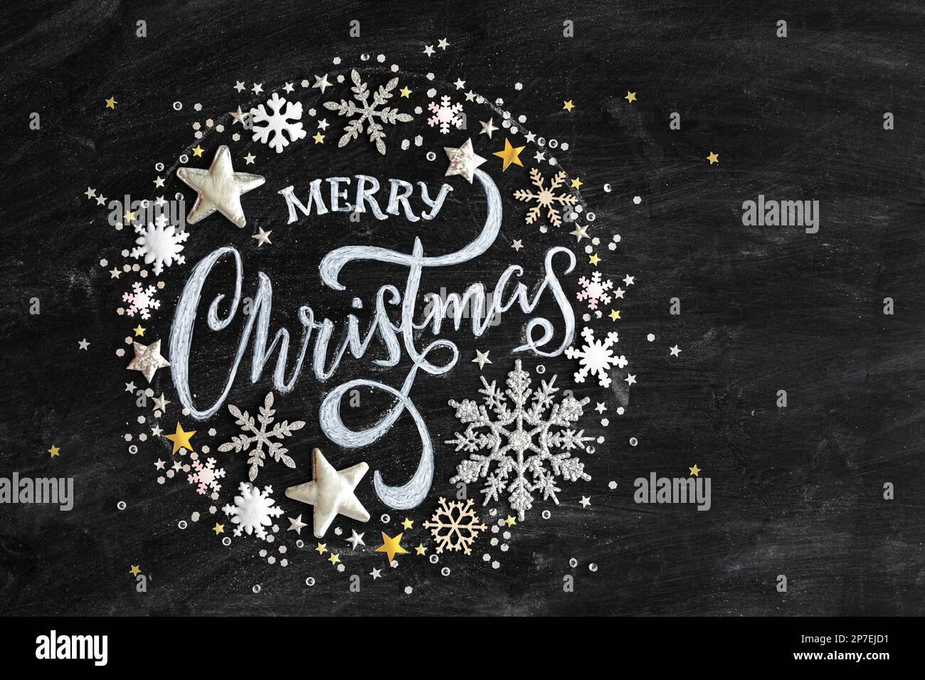 Frohe Weihnachten in Kreide auf einer schwarzen Tafel mit Konfetti und Weihnachtsdekorationen, flach liegend von oben gesehen Stockfoto