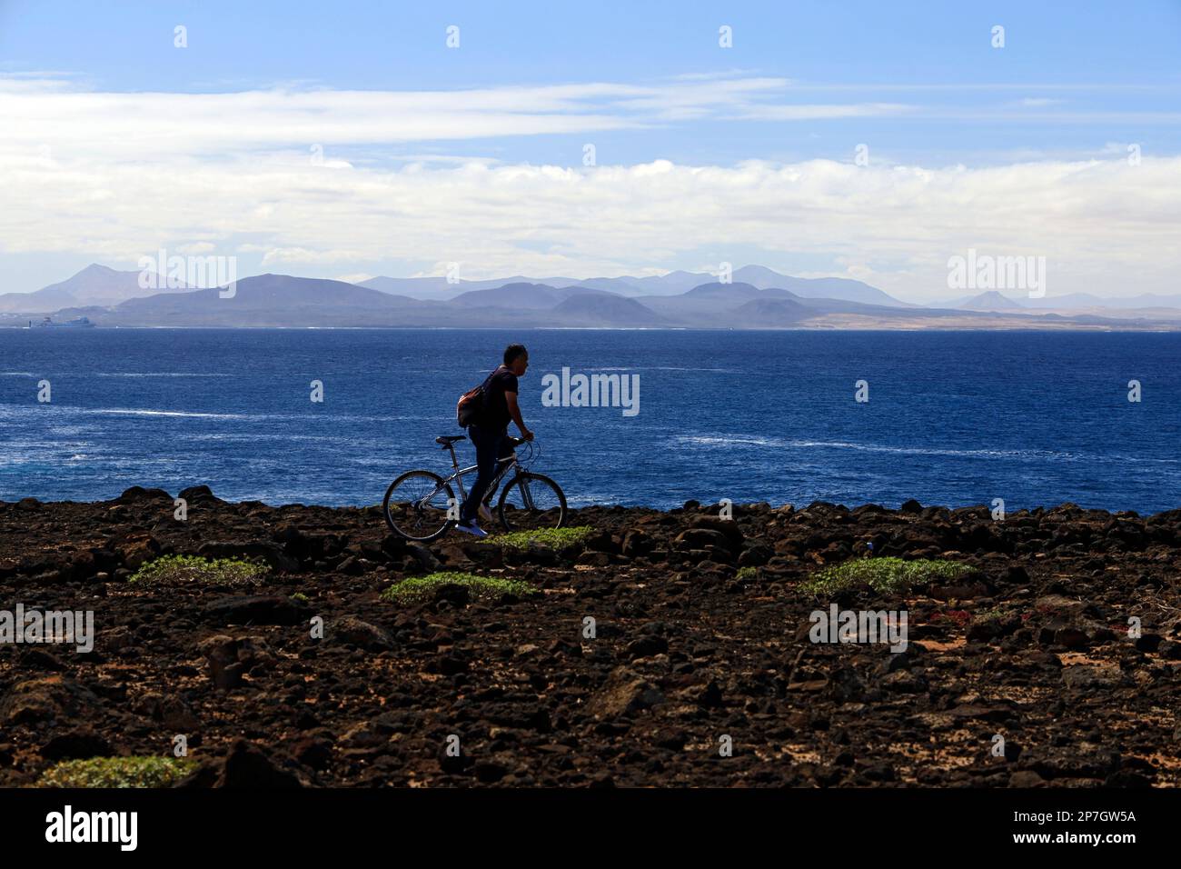 Radfahrer, Playa Blanca mit Fuerteventura in der Ferne, Lanzarote, Kanarische Inseln, Spanien. Stockfoto
