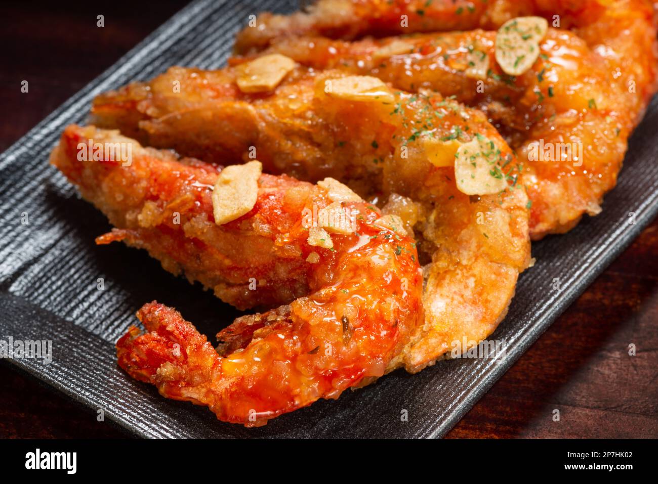 Gegrillte Garnelen in Teig mit Knoblauch in süßer und saurer Sauce auf schwarzem japanischem Teller. Stockfoto
