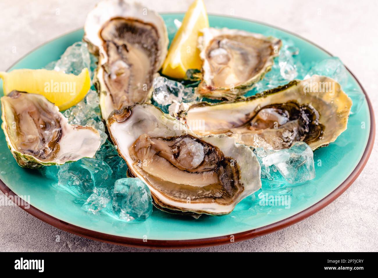 Frische Austern auf blauem Teller, serviert mit Zitrone und Eis. Stockfoto
