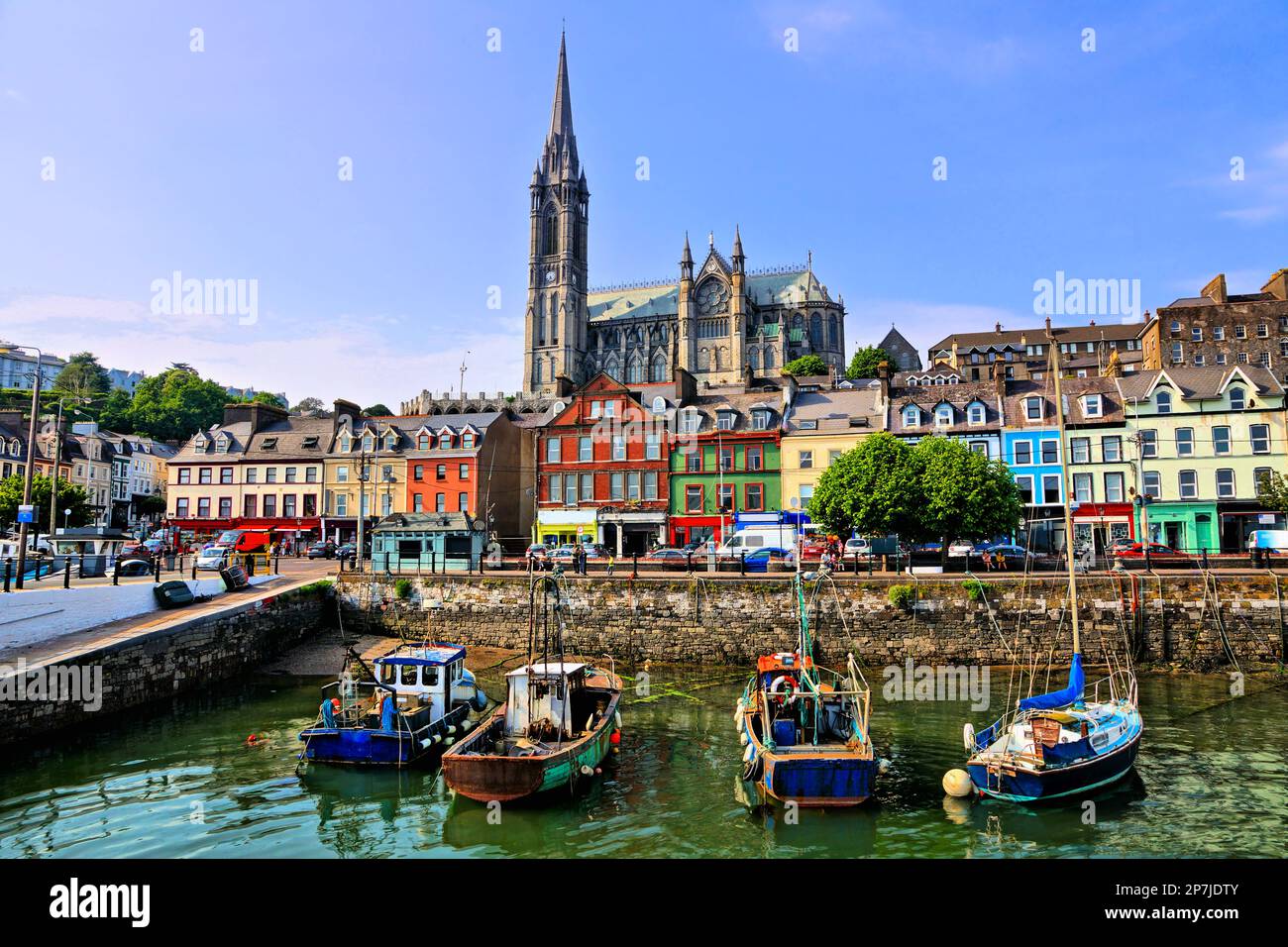 Farbenfrohe Gebäude und alte Boote mit Kathedrale im Hintergrund im Hafen von Cobh, County Cork, Irland Stockfoto