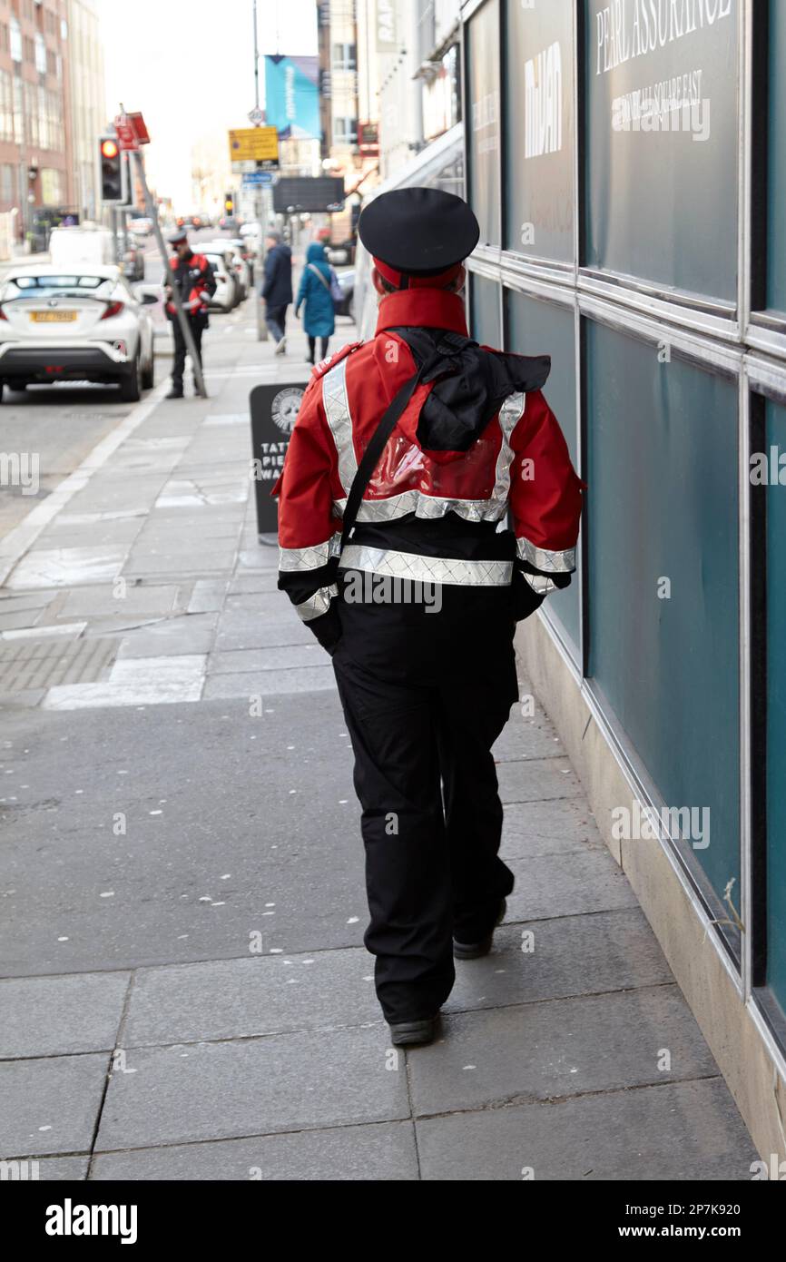 Parkwächter läuft durch das stadtzentrum von belfast, während ein Kollege ein Ticket für ein geparktes Auto im Hintergrund von Belfast Northern Ireland UK ausstellt Stockfoto