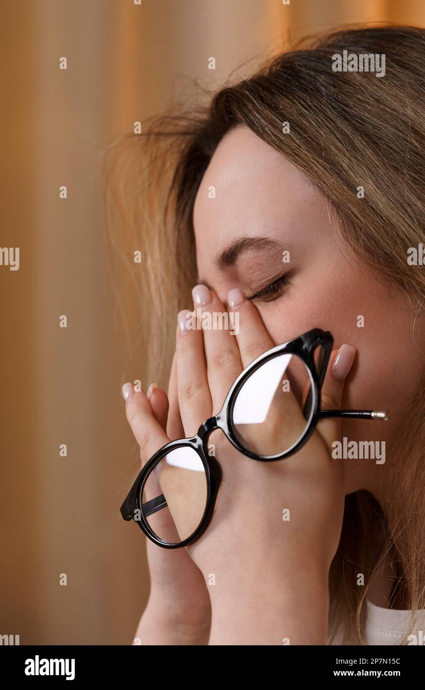 Junge Frau reibt sich die Augen, leidet an Augenmüdigkeit, hält eine Brille in den Augen. Konzepte von Augenkrankheiten. Vertikaler Rahmen. Stockfoto