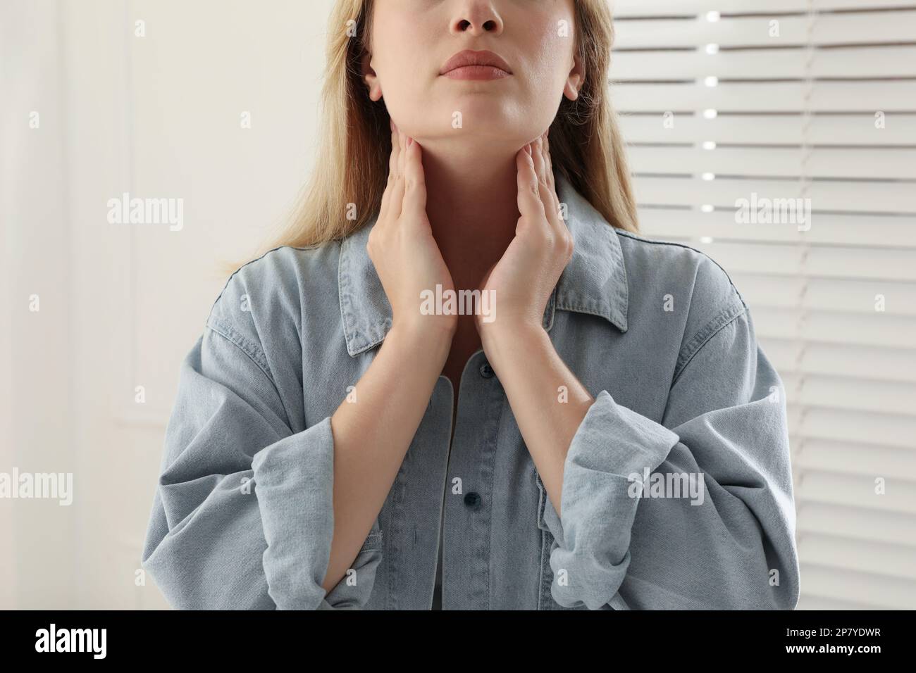 Eine junge Frau, die sich in der Nähe des Fensters im Haus einer Nahaufnahme der Schilddrüse unterzieht Stockfoto