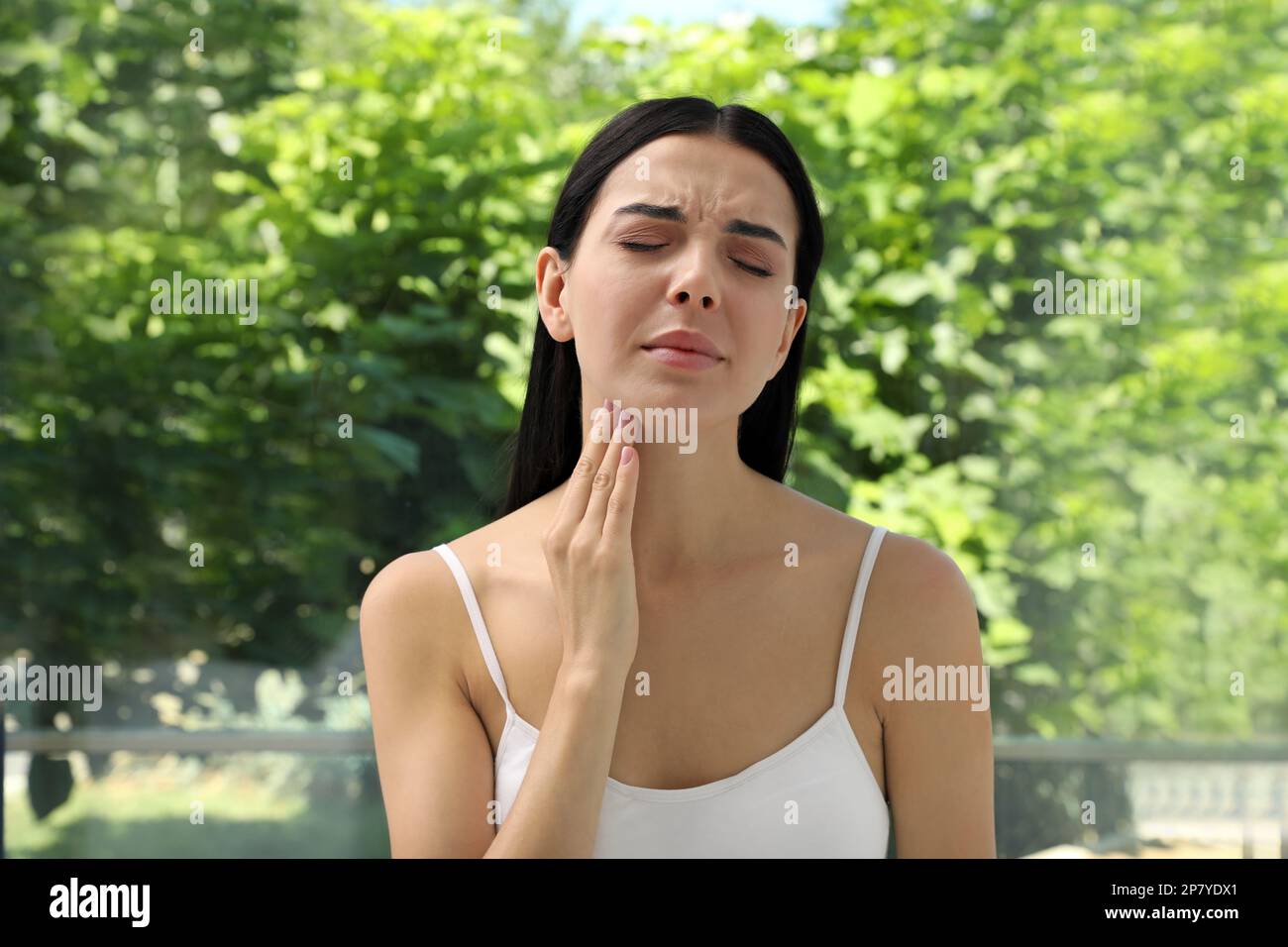 Junge Frau, die Schilddrüsen-Selbstuntersuchung in Fensternähe macht Stockfoto