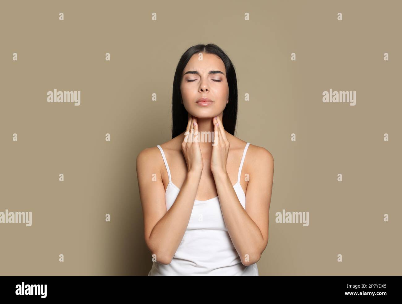 Junge Frau, die Schilddrüsen-Selbstuntersuchung auf beigefarbenem Hintergrund macht Stockfoto