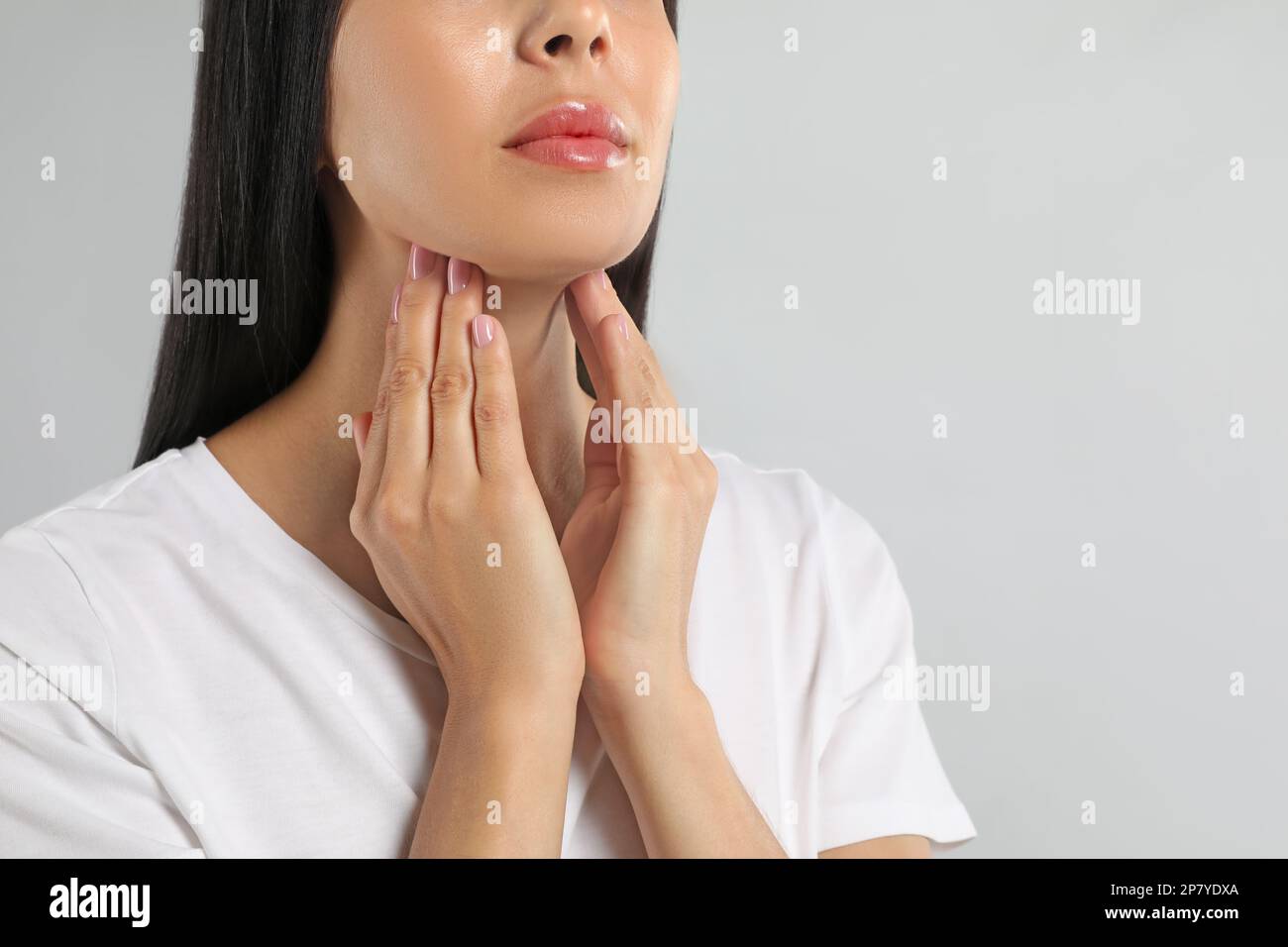 Junge Frau, die Schilddrüsen-Selbstuntersuchung vor hellem Hintergrund macht, Nahaufnahme Stockfoto