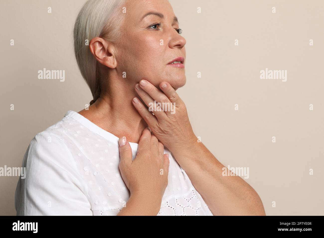 Reife Frau, die Schilddrüsen-Selbstuntersuchung auf beigefarbenem Hintergrund macht Stockfoto