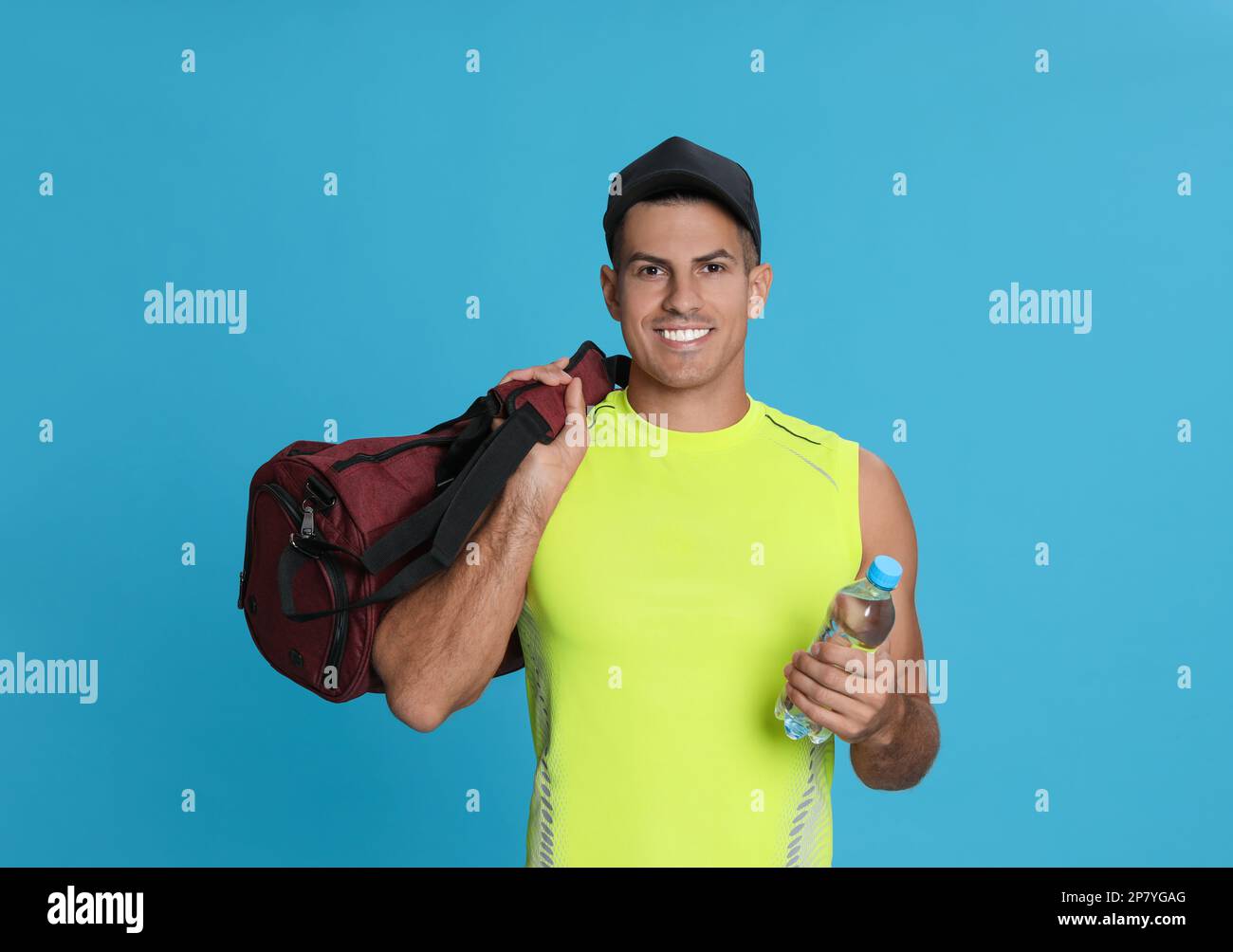 Ein gutaussehender Mann mit Sporttasche und einer Flasche Wasser auf hellblauem Hintergrund Stockfoto