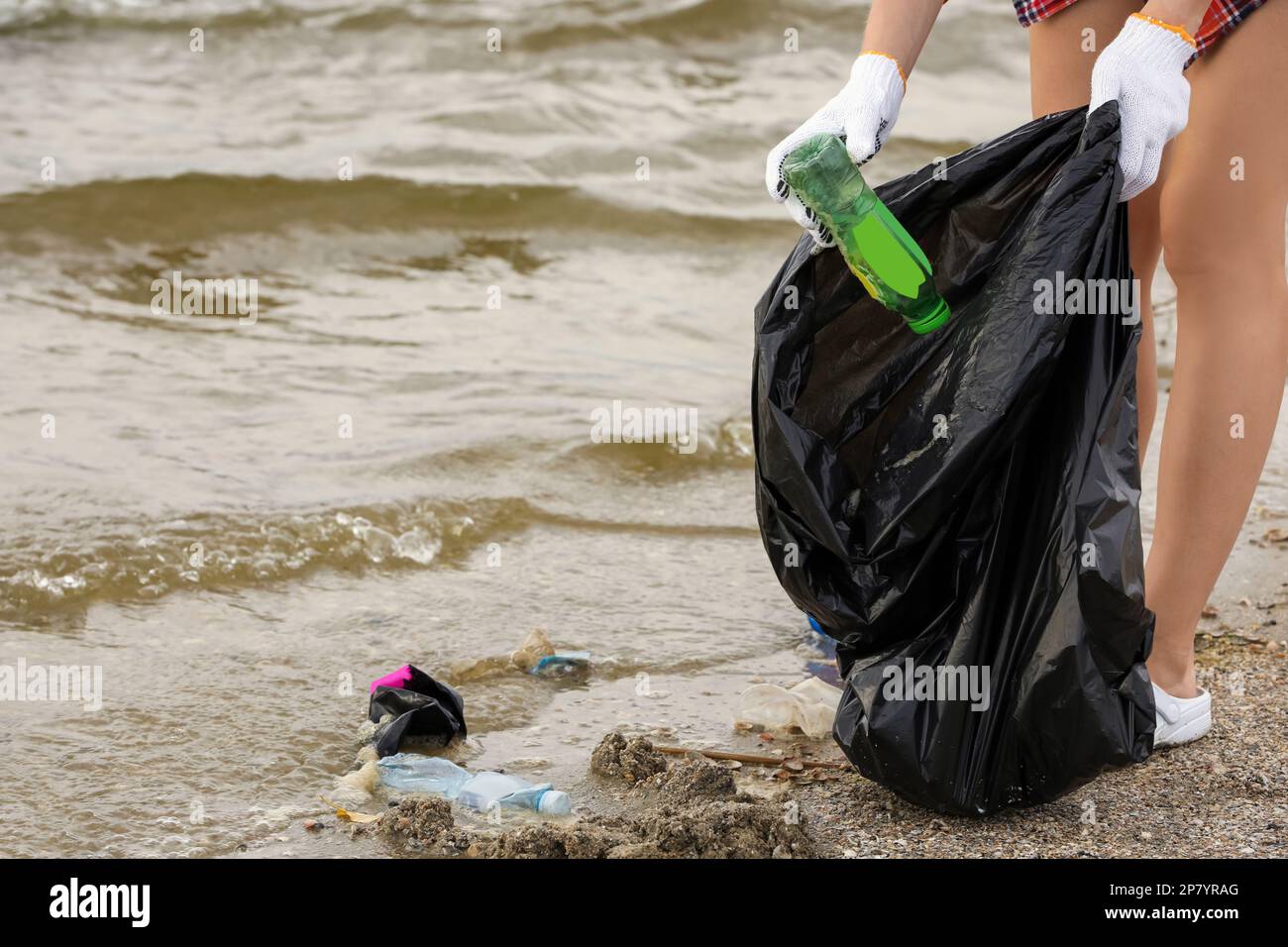 Frau in Handschuhen mit Müllsack, Müll am Strand einsammeln, schließen Stockfoto