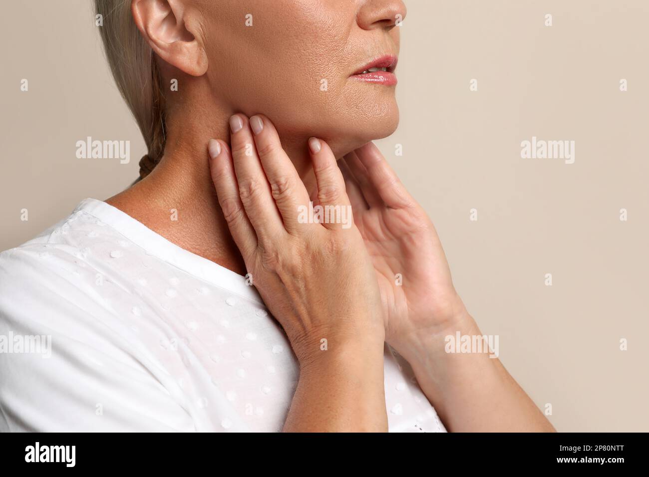 Reife Frau, die Schilddrüsen-Selbstuntersuchung bei beigefarbener Hintergrundnaht macht Stockfoto