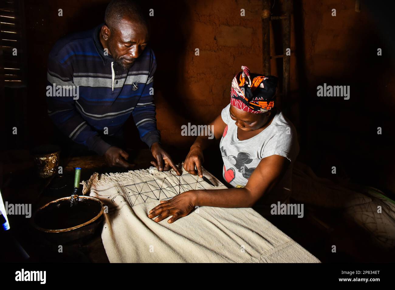 (230309) -- YAOUNDE, 9. März 2023 (Xinhua) -- Flore Amedite Kammogne, unterstützt von ihrem Ehemann, zeichnet Muster auf einem Stoff, um den traditionellen Ndop in ihrer Werkstatt in Baham, Kamerun, am 3. März 2023 zu machen. In Kamerun waren Kunsthandwerk wie Nähen, Steppnähen, Stickereien und Stricken schon immer ein Ventil für Frauen, um ihre Kreativität zu nutzen. Ndop-Material wurde ursprünglich von Frauen hergestellt und war ein wichtiges Symbol für sozialen Status und kulturelles Erbe, aber heute - auf eine andere Weise - verbessert es das Leben von Frauen.MIT dem Motto "Feature: Ndop-Material verwandelt Frauen in Kleinstunternehmer in Cam Stockfoto