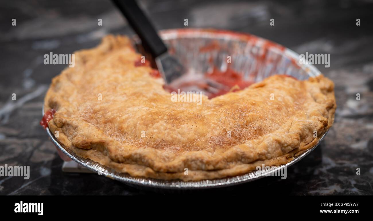 Kruste eines frischen, köstlichen Erdbeer-Rhabarberkuchen in einer Aluminiumdose, mit Granulaten Suger im selektiven Fokus, nachdem ein Spatel verwendet wurde, um p zu entfernen Stockfoto