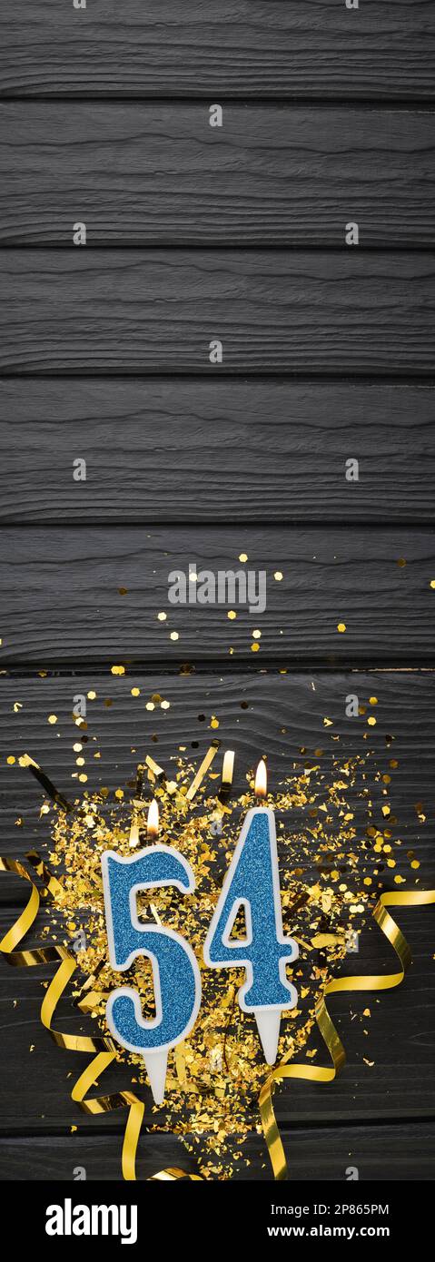 Blaue Festkerze Nummer 54 und goldene Konfetti auf dunklem Holzhintergrund. 54. Geburtstagskarte. Jubiläums- und Geburtstags Vertikales Banner. Stockfoto